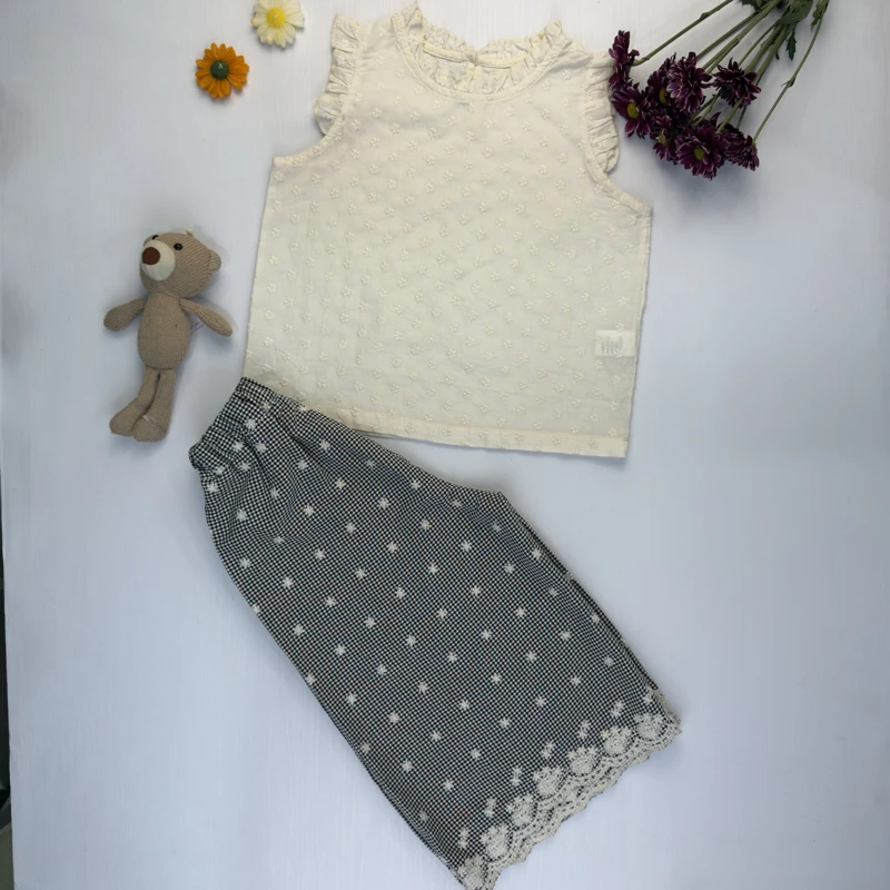 ست بلوز آستین حلقه‌ای کرم و شلوار چهارخانه گیپور دار دخترانه روی زمینه سفید.