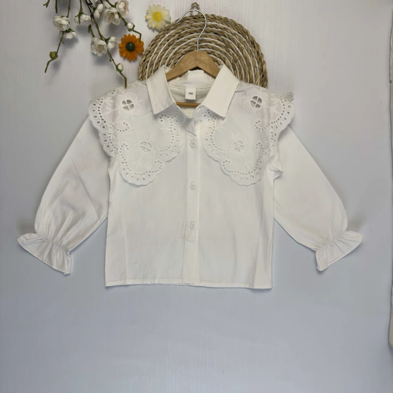 شومیز سفید دخترانه با یقه توری بزرگ و گلدوزی شده روی چوب لباسی.