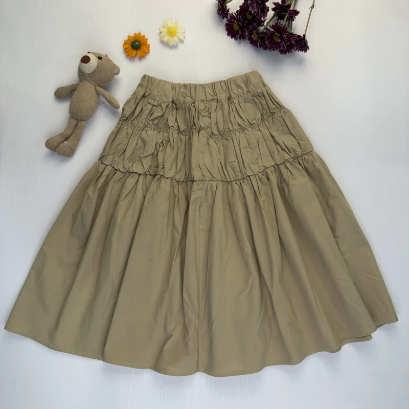 دامن دخترانه نخی رنگ کرم خاکی با مدل چین‌دار و طبقاتی روی پس‌زمینه سفید.