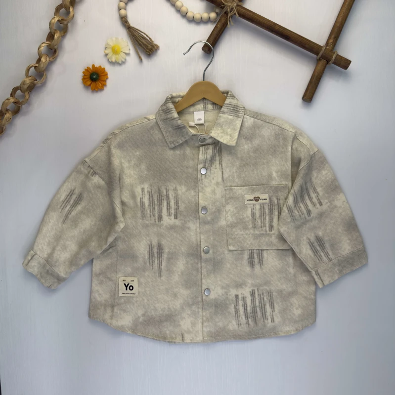 نمای کامل پیراهن کتان کبریتی بچگانه طرح ابروبادی کرم و طوسی روی چوب لباسی.