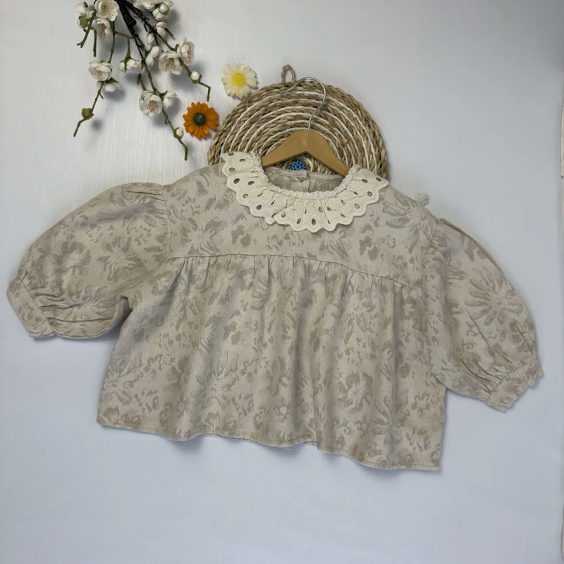 شومیز دخترانه رنگ کرم با یقه بزرگ توری و خامه‌دوزی شده روی زمینه سفید.