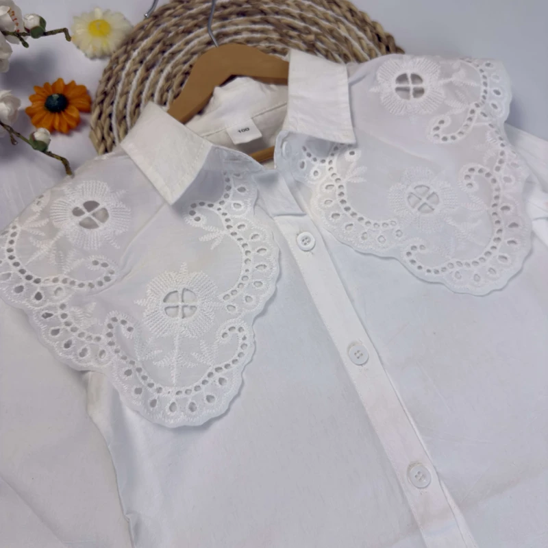 نمای نزدیک از طرح خامه دوزی و دالبرهای یقه بلوز دخترانه سفید.