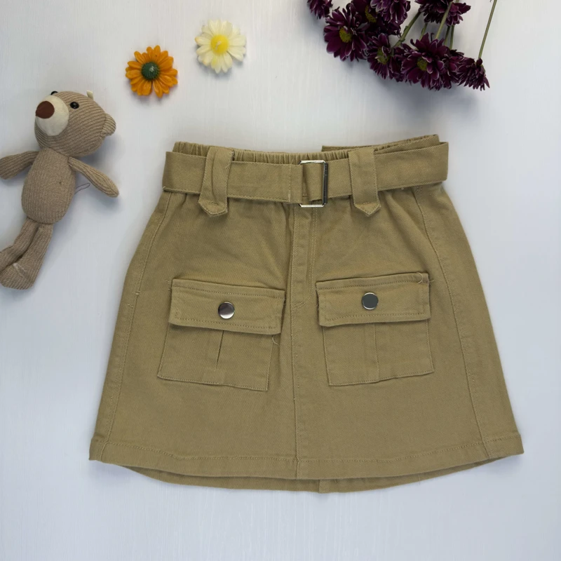 دامن کتان دخترانه رنگ کرم با کمربند و جیب‌های پاکتی روی زمینه سفید.