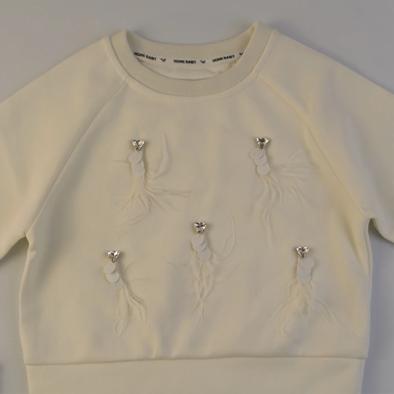 نمای نزدیک تزیینات پر و مروارید روی بلوز دخترانه